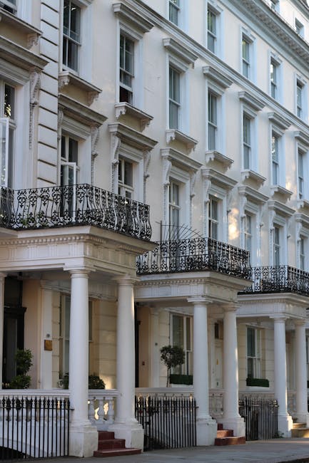A street scene in Belgravia featuring a row of elegant, white terraced townhouses with decorative architectural details and large sash windows. Several leafless trees line the pavement, casting shadow